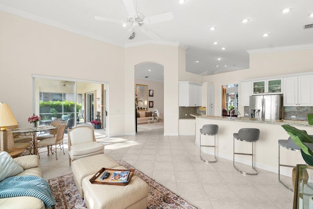 living room featuring ceiling fan, arched walkways, crown molding, and light tile patterned floors