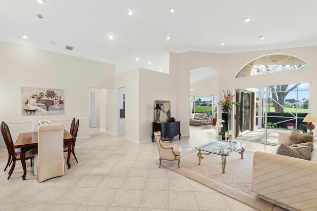 living room with visible vents, arched walkways, a towering ceiling, crown molding, and light tile patterned flooring