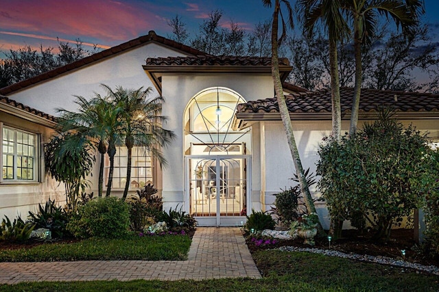 exterior entry at dusk featuring a tile roof and stucco siding