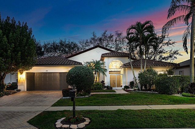 mediterranean / spanish-style house with a garage, a tile roof, decorative driveway, and stucco siding