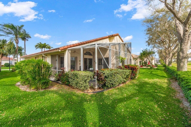 back of property with a yard, a lanai, a tiled roof, and stucco siding