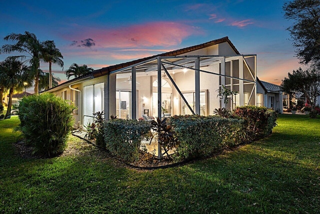 property exterior at dusk featuring glass enclosure and a yard