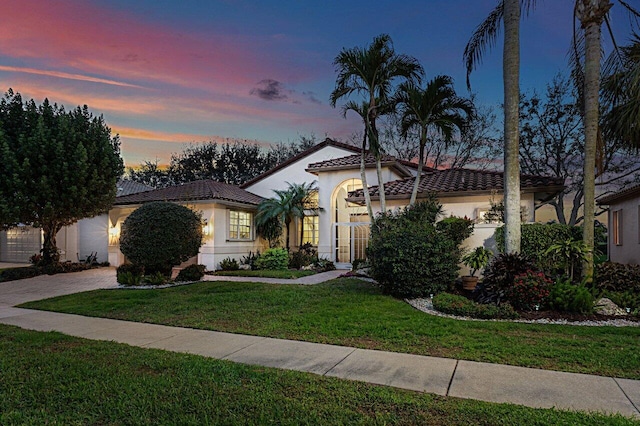 mediterranean / spanish-style home with stucco siding, a tile roof, decorative driveway, and a front yard