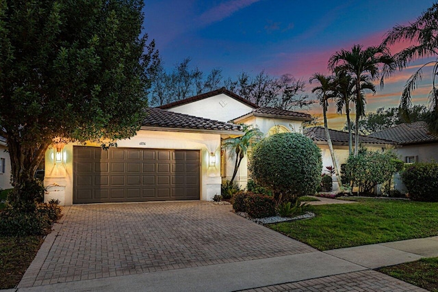 mediterranean / spanish-style home featuring a tile roof, an attached garage, decorative driveway, a front lawn, and stucco siding