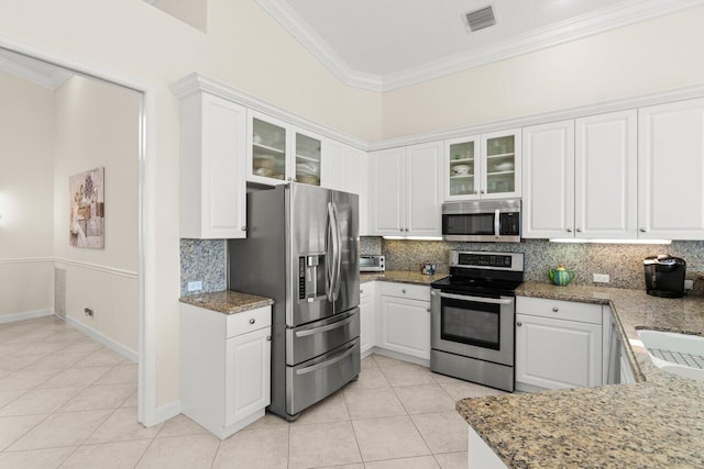 kitchen featuring stone counters, appliances with stainless steel finishes, glass insert cabinets, ornamental molding, and white cabinetry