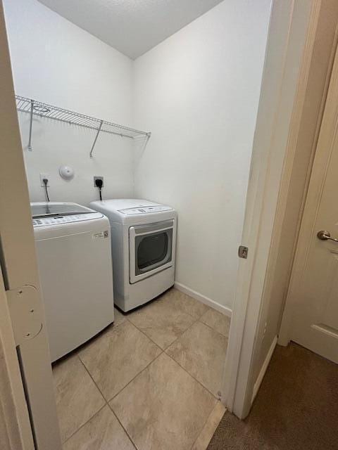 laundry room featuring light tile patterned floors, laundry area, washing machine and dryer, and baseboards