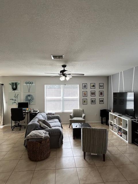 living area featuring a ceiling fan, visible vents, a textured ceiling, and light tile patterned floors