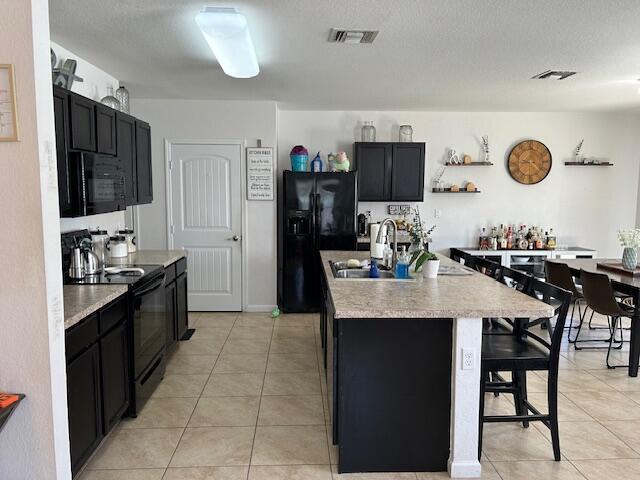 kitchen featuring a breakfast bar area, light tile patterned flooring, dark cabinets, light countertops, and black appliances