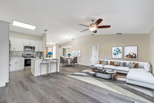 living area with ceiling fan with notable chandelier, visible vents, vaulted ceiling, and wood finished floors