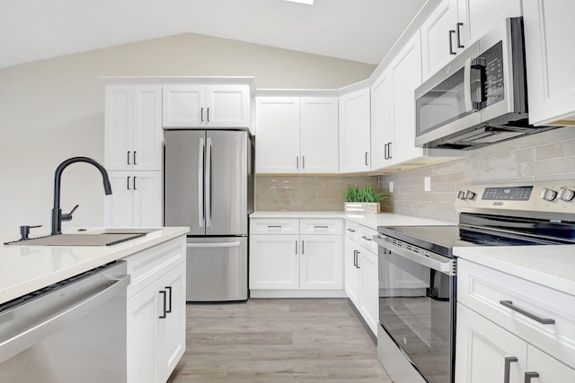 kitchen with white cabinets, vaulted ceiling, stainless steel appliances, light countertops, and a sink