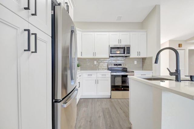 kitchen featuring tasteful backsplash, light countertops, appliances with stainless steel finishes, white cabinetry, and a sink