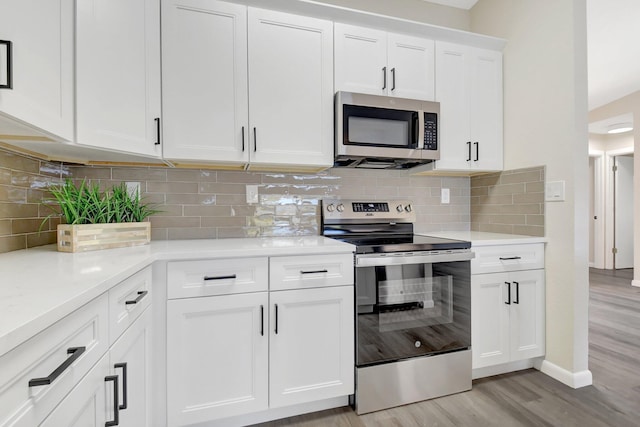 kitchen featuring baseboards, appliances with stainless steel finishes, light wood-type flooring, white cabinetry, and backsplash