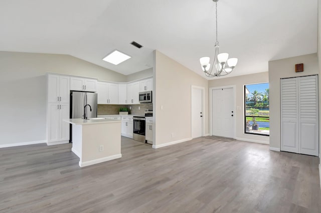 kitchen featuring a kitchen island with sink, white cabinets, light countertops, appliances with stainless steel finishes, and decorative light fixtures