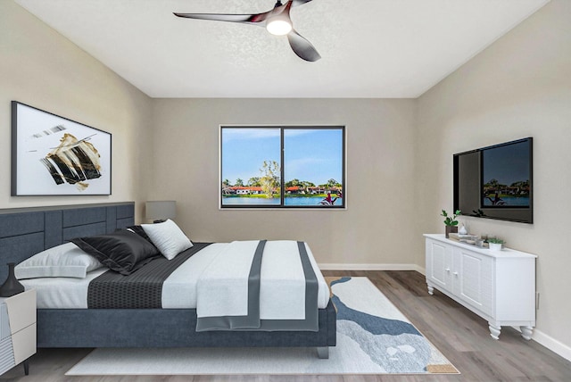 bedroom with ceiling fan, a textured ceiling, baseboards, and wood finished floors