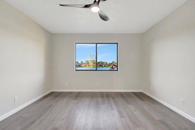 empty room with a textured ceiling, light wood-type flooring, a ceiling fan, and baseboards