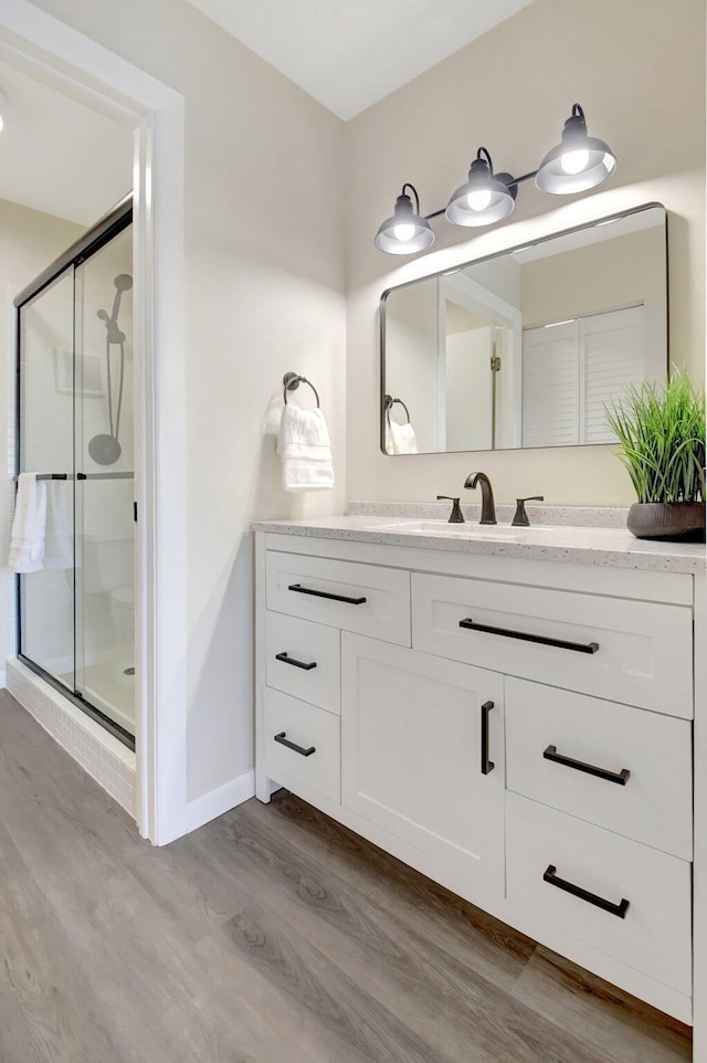 full bath with a shower stall, baseboards, wood finished floors, and vanity