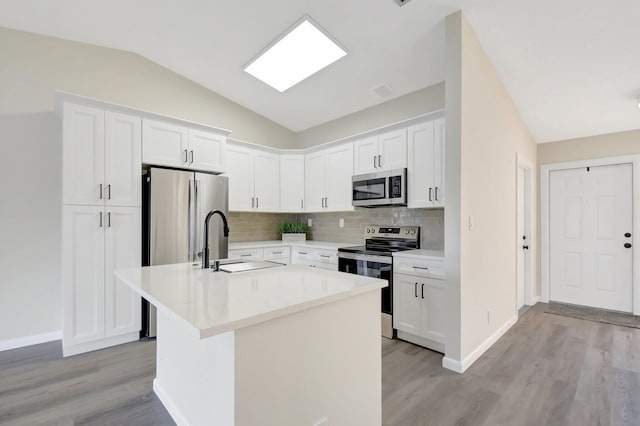 kitchen with lofted ceiling, a kitchen island with sink, stainless steel appliances, white cabinetry, and light countertops