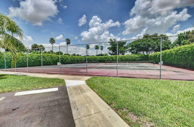 view of tennis court featuring fence and a yard