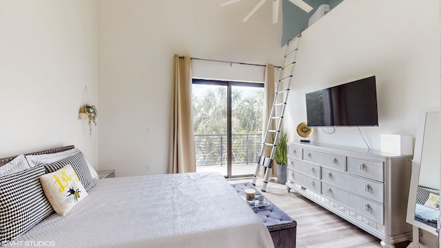 bedroom featuring access to exterior, light wood-type flooring, and a high ceiling