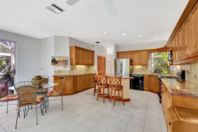 kitchen featuring a center island, a breakfast bar area, visible vents, ceiling fan, and black appliances