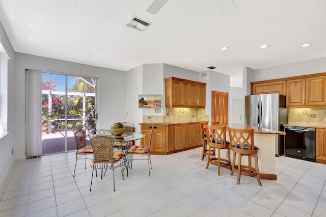 kitchen with black dishwasher, visible vents, light stone counters, a breakfast bar area, and a center island