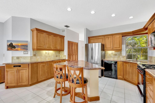 kitchen with light tile patterned floors, light stone counters, a kitchen island, visible vents, and black appliances