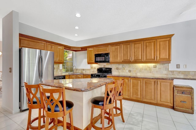 kitchen featuring stone countertops, a breakfast bar, a sink, black appliances, and backsplash