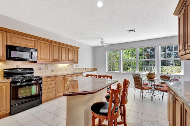 kitchen featuring a breakfast bar area, light tile patterned floors, tasteful backsplash, visible vents, and black appliances