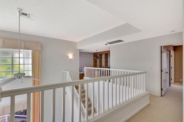 hall featuring carpet floors, visible vents, a textured ceiling, and an upstairs landing