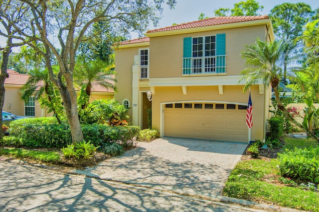 mediterranean / spanish-style home featuring a tiled roof, decorative driveway, an attached garage, and stucco siding