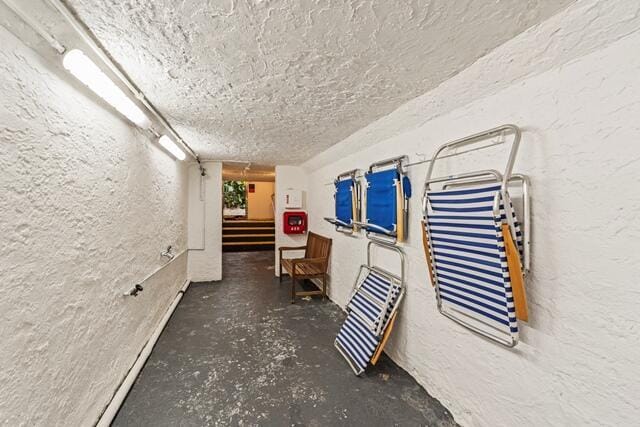 hallway with a textured ceiling, a textured wall, and unfinished concrete flooring