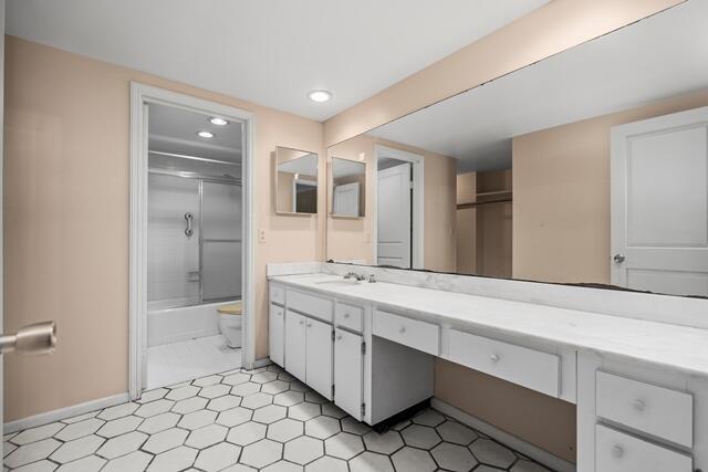 bathroom featuring recessed lighting, toilet, combined bath / shower with glass door, vanity, and baseboards