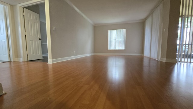 empty room with crown molding, baseboards, and wood finished floors