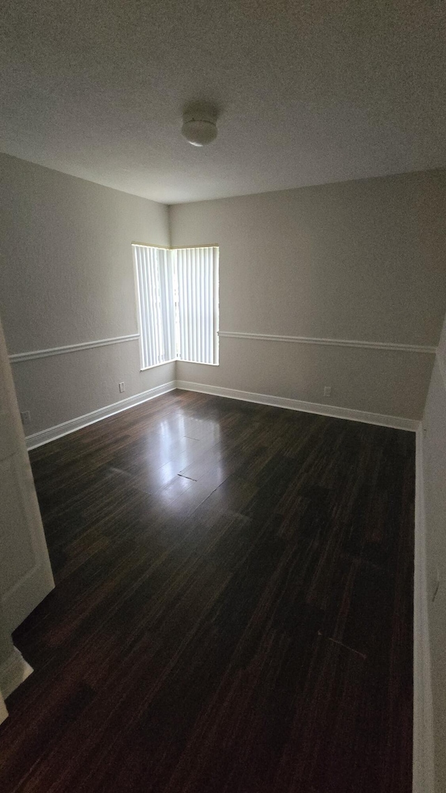 unfurnished room featuring a textured ceiling, dark wood finished floors, and baseboards