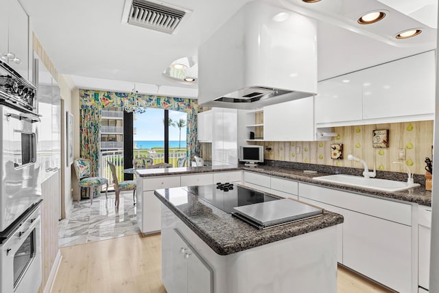 kitchen with visible vents, a sink, exhaust hood, white cabinets, and stainless steel oven