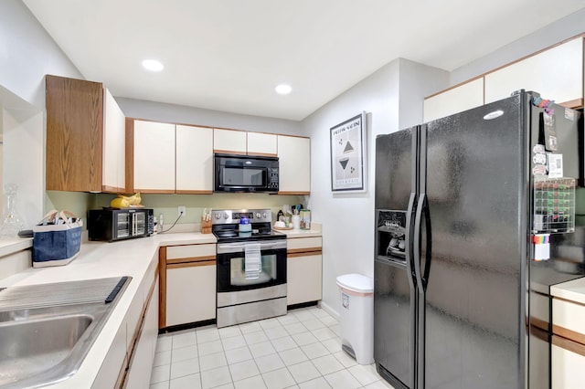 kitchen with light tile patterned floors, white cabinets, light countertops, black appliances, and a sink