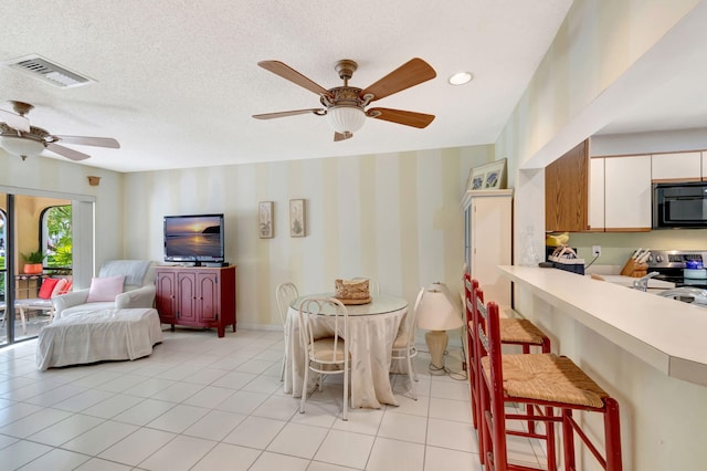 dining room with light tile patterned floors, visible vents, ceiling fan, a textured ceiling, and wallpapered walls