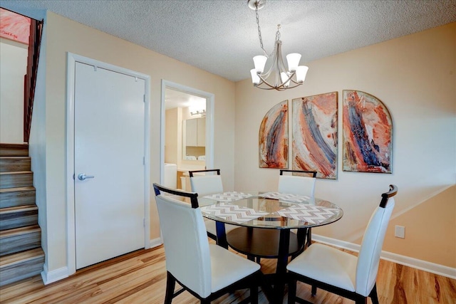 dining room with a chandelier, stairway, light wood-style flooring, and a textured ceiling