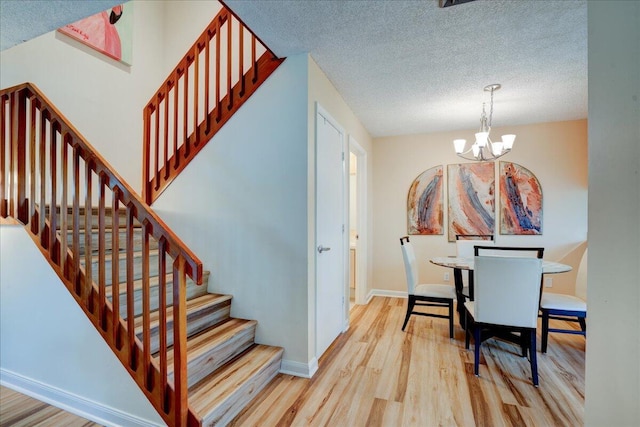 stairs with an inviting chandelier, a textured ceiling, baseboards, and wood finished floors