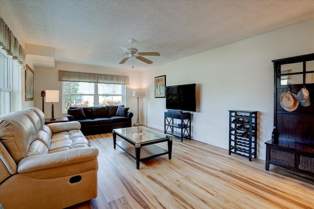 living area featuring light wood-type flooring, ceiling fan, a textured ceiling, and baseboards