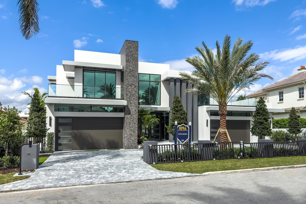 modern home with a garage, decorative driveway, fence, and stucco siding