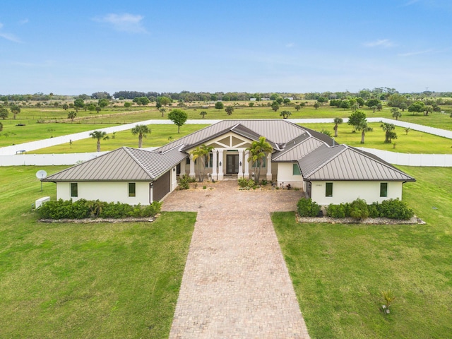 view of front of house featuring metal roof, a rural view, a standing seam roof, decorative driveway, and stucco siding