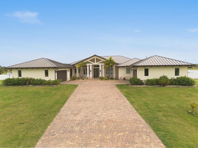 view of front of property with decorative driveway, a standing seam roof, a front lawn, and stucco siding