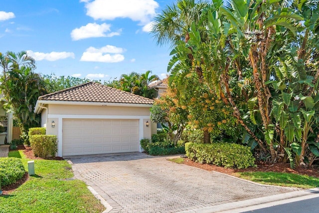 mediterranean / spanish-style home with decorative driveway, a tile roof, an attached garage, and stucco siding