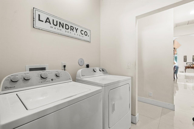 clothes washing area featuring laundry area, light tile patterned flooring, washer and clothes dryer, and baseboards