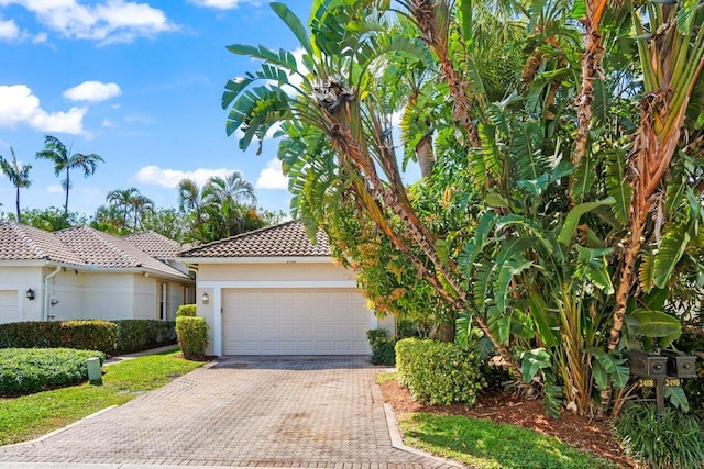 view of front of property featuring a garage, decorative driveway, a tile roof, and stucco siding