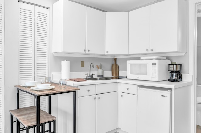 kitchen with white microwave, refrigerator, a sink, white cabinetry, and light countertops