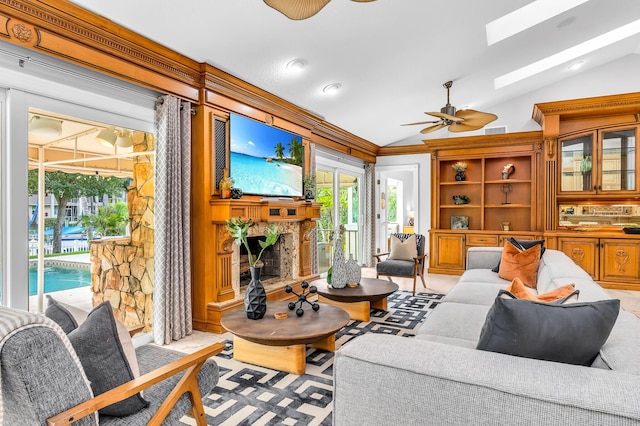 living room with lofted ceiling with skylight, visible vents, ceiling fan, and a stone fireplace