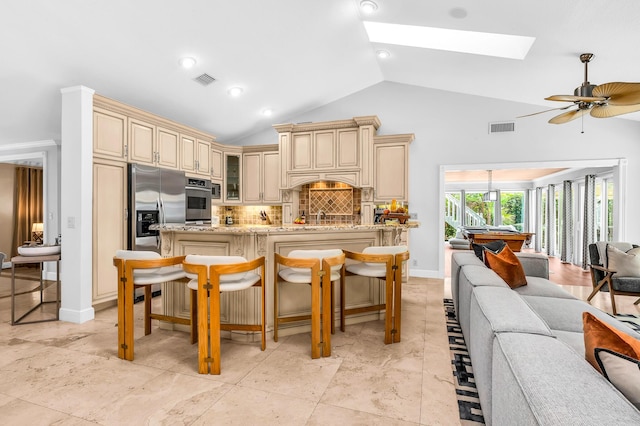 kitchen with a breakfast bar area, cream cabinets, glass insert cabinets, appliances with stainless steel finishes, and open floor plan