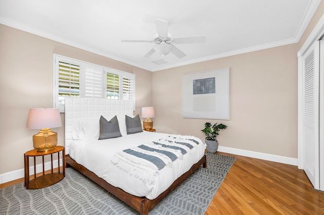 bedroom with a closet, ornamental molding, ceiling fan, wood finished floors, and baseboards